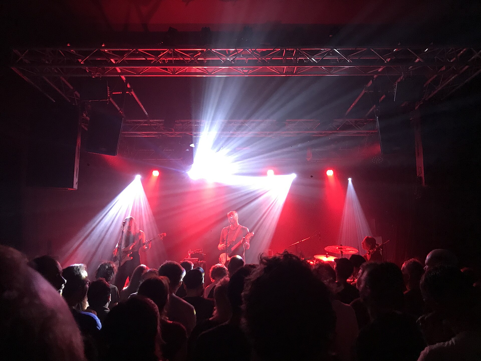A band performs live on stage with red lighting and a large crowd enjoying the show, reflecting television's role in shared.