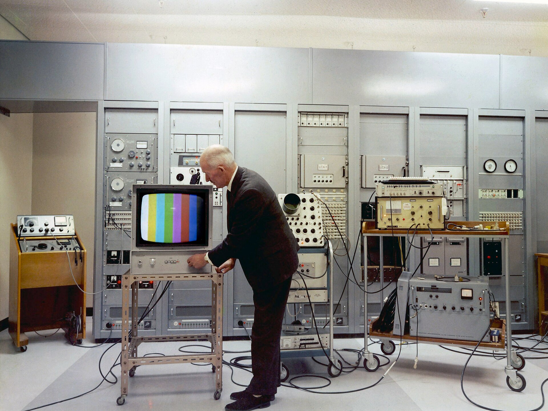A man examines a vintage television showing test patterns in an electronics control room.